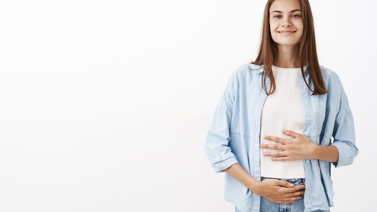 Mujer sonriente que se toca el vientre representando que sigue las estrategias para una digestión sana.