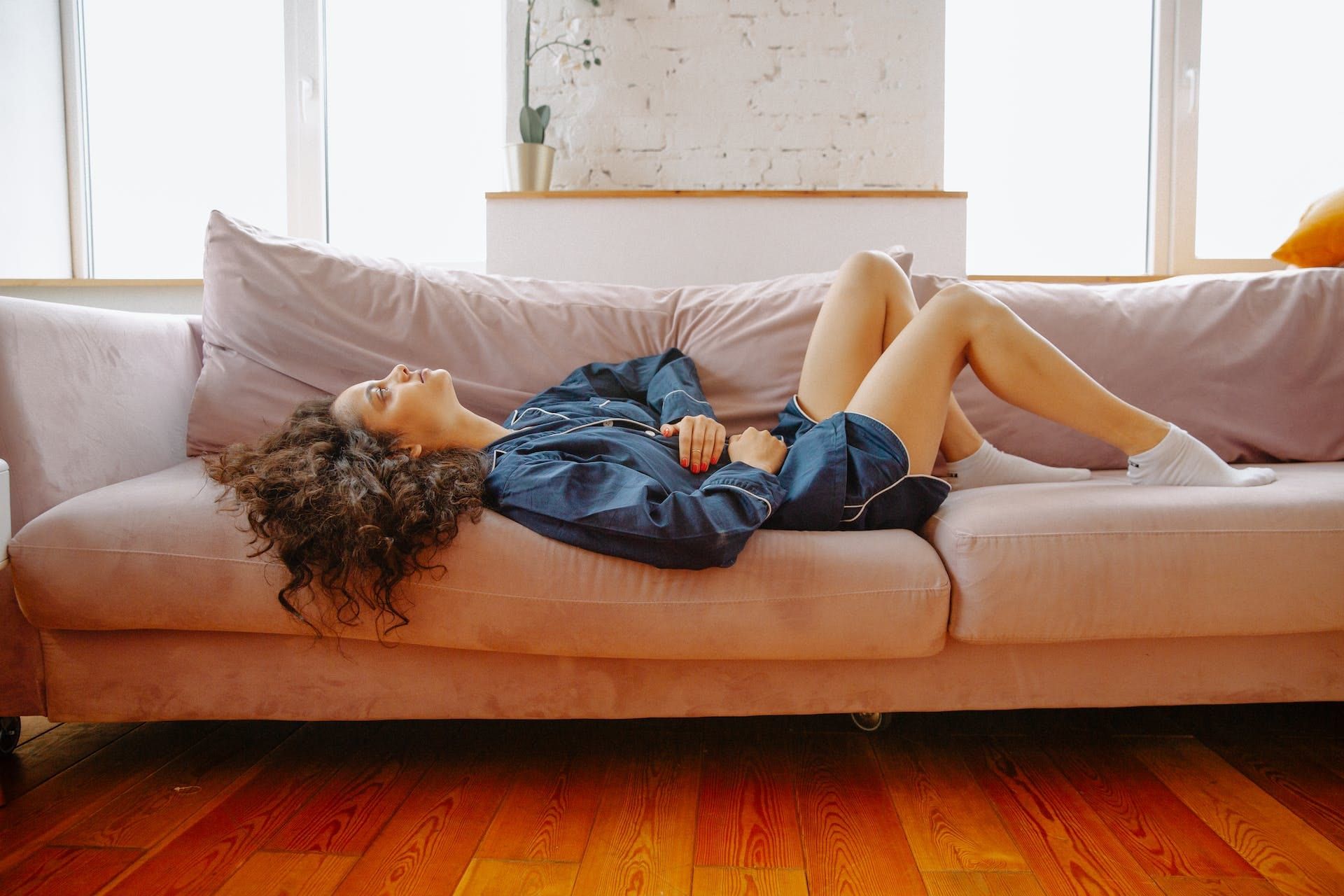 Mujer experimentando dolor menstrual tirada en el sofá antes de realizar remedios naturales para  el dolor menstrual